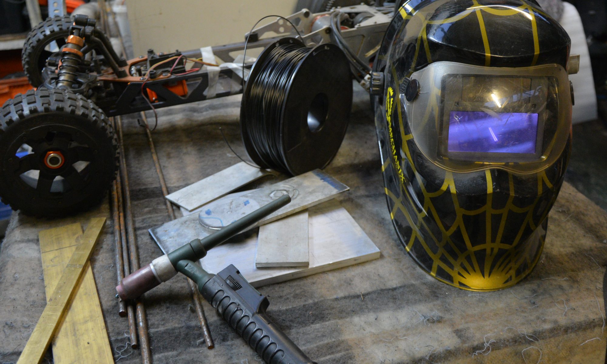 on the work bench is a welding tourch, welding helmet and various bits of metal